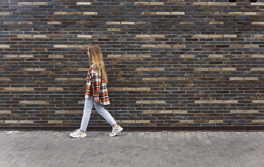 young woman walks down the street against a brick wall