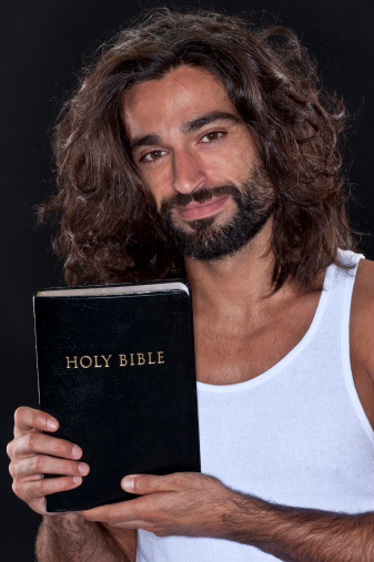 Bearded mid adult man holding his bible looking at the camera on black background