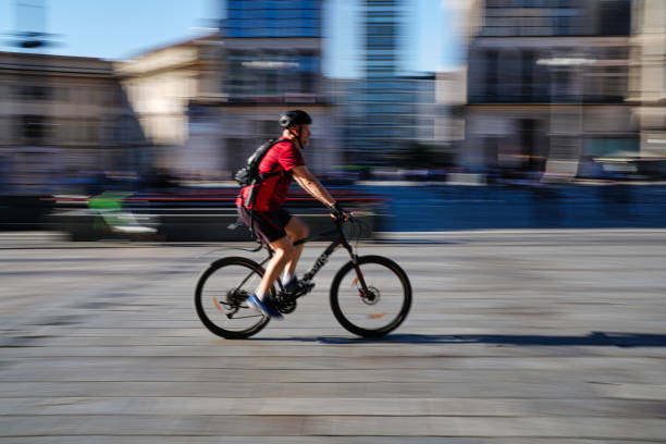 Milan, Italy - August 10, 2023: people cross piazza del duomo by bicycle
