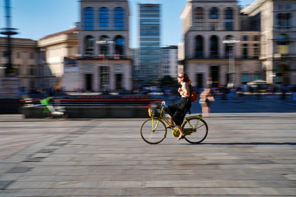 Milan, Italy - August 10, 2023: people cross piazza del duomo by bicycle