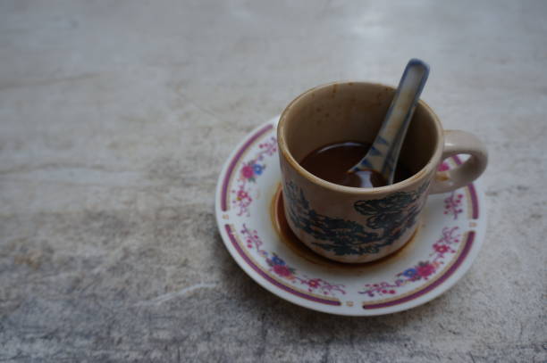 istock Traditional black coffee in ceramic cup with saucer, spoon, and authentic transfer print pattern design. Coffee cup on a saucer. Coffee leaked on the saucer. Half consumed coffee with a spoon inside the ceramic cup. Traditional authentic ceramic cup. 1605546368