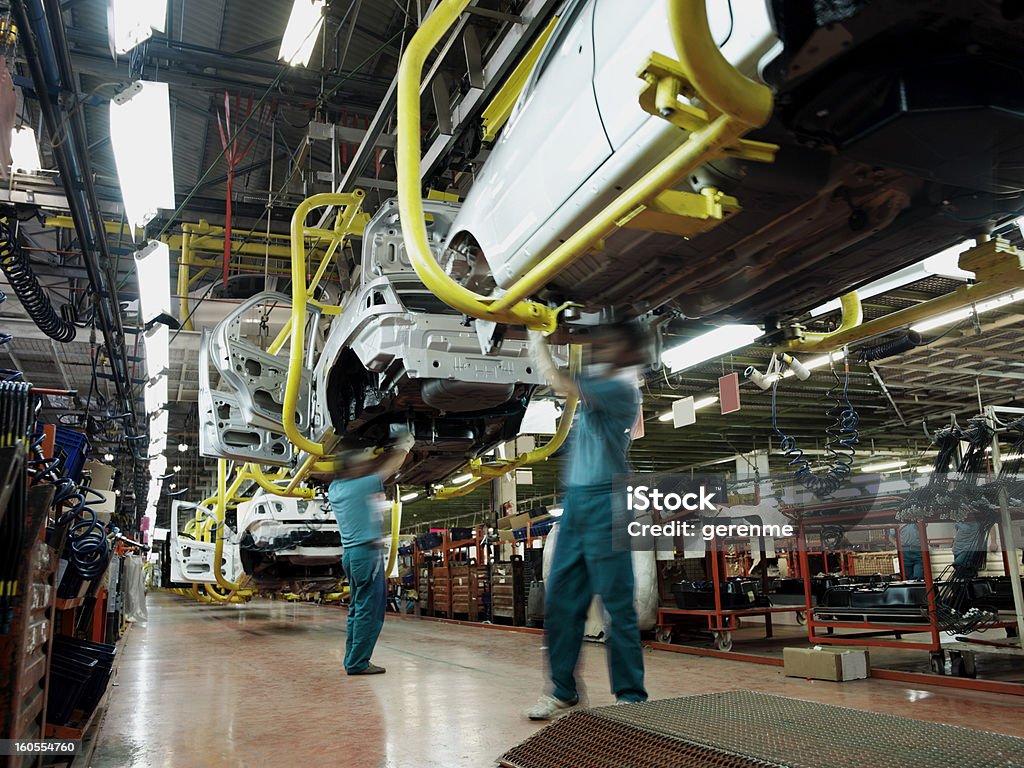 Car factory production line Two workers wearing green shirts and blue pants work underneath a car in an automobile factory.  There are assembly lines, partially constructed cars, tools and electrical equipment in the background. Car Stock Photo