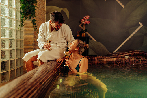 Beautiful woman and young couple relaxing in hot tub at health spa with her husband in bathrobe who sitting beside