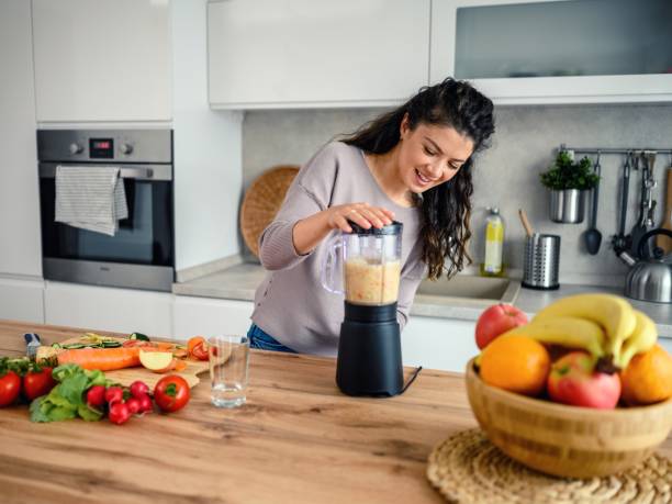 istock Woman preparing a smoothie in her kitchen at home 1605585968