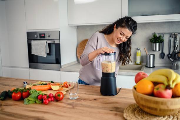 istock Woman preparing a smoothie in her kitchen at home 1605590738