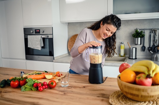Woman smiling happily while preparing a smoothie in her kitchen at home