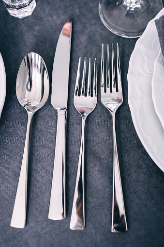 On a gray napkin are shiny new cutlery, silverware next to a white plate.