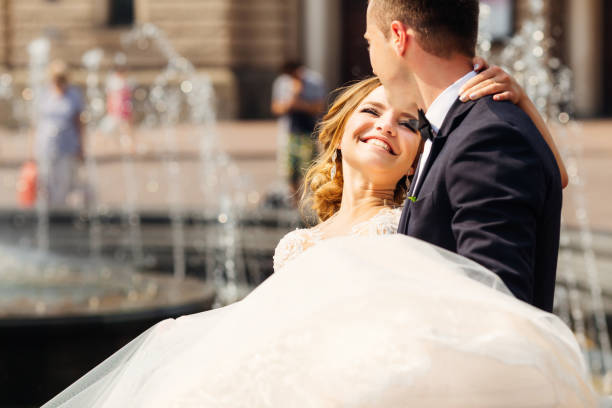 Bride and groom in the park by the fountain on clear summer day. Happy newlyweds embrace in a summer park.