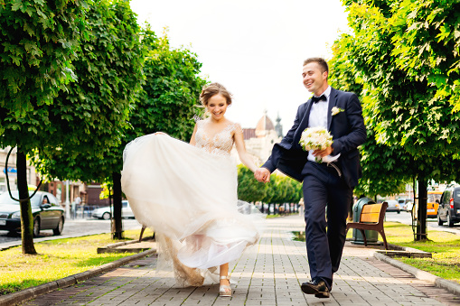 the newlyweds hold their hands and running along the pavement and have fun laughing