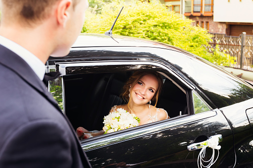 Bride sitting in a black car and looking at her fiance through a window