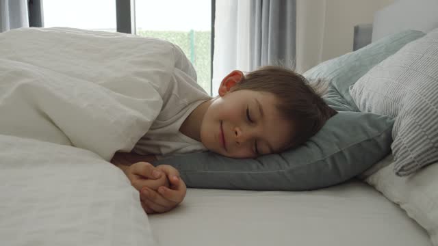 Little boy sleeping and smiling in bed. Automatic blinds open and let the light in the bedroom.