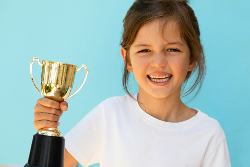 Little girl raising a winning glass one hand, on blue background.