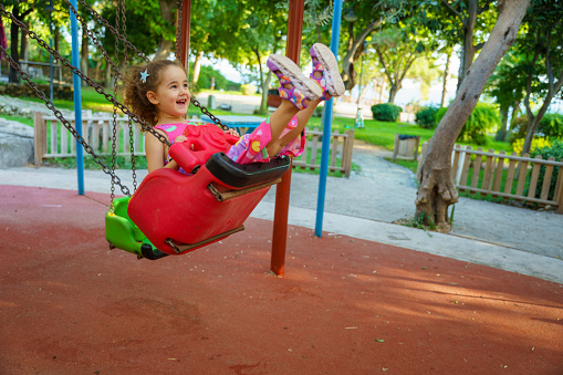 Happy little girl kid having fun on the swing. Little girl child wearing red dress having fun in a fun park