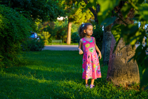 Sweet, happy little girl sitting on a grass in a park at a spring stream with flower in hand. Laughing, enjoying fresh air in forrest.