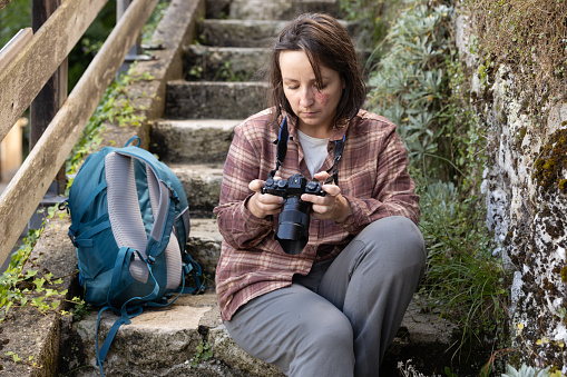Portrait of a female photographer sitting on a stone staircase and viewing photos on a camera. High quality photo