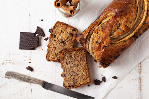 Sliced moist banana bread with oats and dark chocolate chunks on a white wooden table