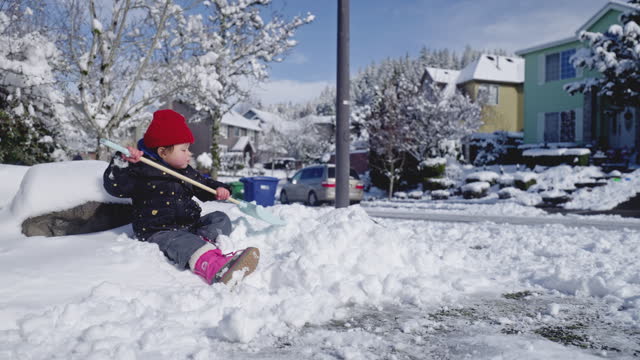 Young daughter helps mother shovel snow off their driveway