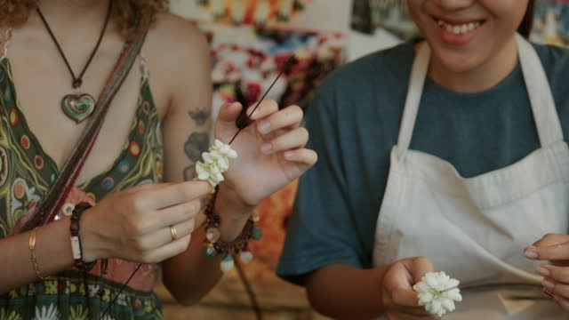 Close-up shot of Thai women making flower garlands with their hands at the shop.