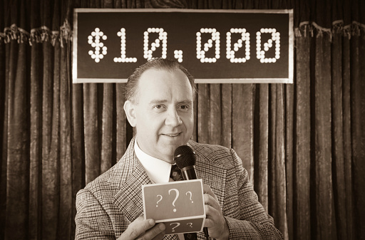 A vintage processed game show host holding a microphone. Photographed in studio with a purpose built set and props.