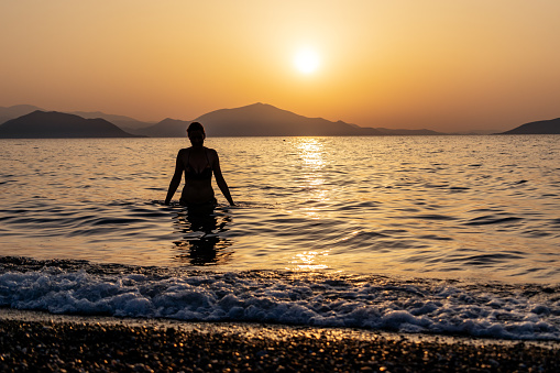 Silhouette of a woman entering the sea or ocean at sunset. Copy space.