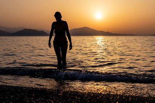 Silhouette of a woman stepping out of the sea or ocean at sunset. Copy space.