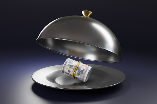 US bankroll on a black plate covered by a silver metal cloche on dark purple background. Illustration of the concept of fine dining and middle class gourmet