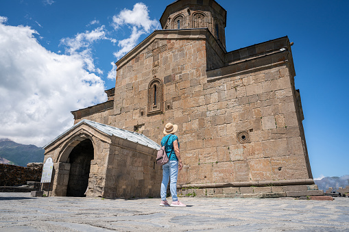 Elderly tourist woman wit backpack visiting the old Gergeti Trinity Church in Kazbegi,Georgia