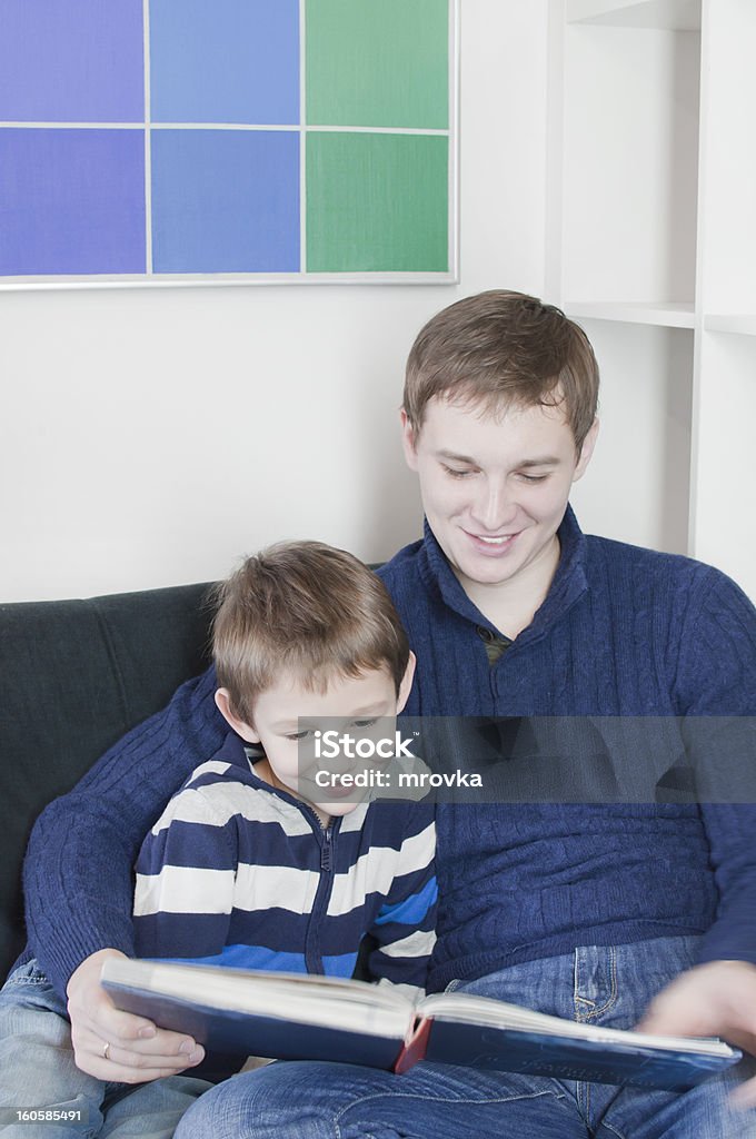 Family Young father with his son sit on the sofa and watch a book Boys Stock Photo