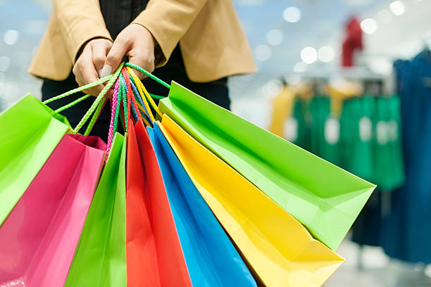 colorful shopping bags being held on blurry mall background - çok sayıda nesne stok fotoğraflar ve resimler