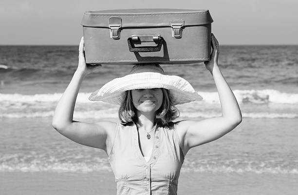 young woman standing on the beach with vintage suitcase