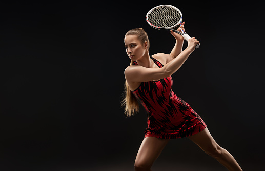 Woman tennis player dressed in sports gown is demonstrating professional skills. Professional tennis player is holding racket in attacking position. Dynamic pose. Beauty of tennis.