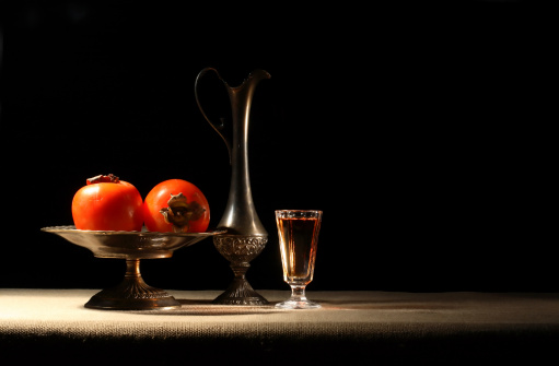 Antique vases with persommons near glass of wine on dark background