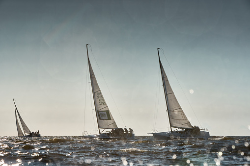Russia, St.Petersburg, 07 July 2023: The sailing race, few boats in a roll go at high speed, sailing boats are in regatta at sunset, handsome sailors on the board of yacht, wind and splashes. High quality photo