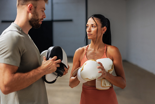 Fitness instructor and an athlete having a discussion while holding boxing gloves and preparing for training at the gym