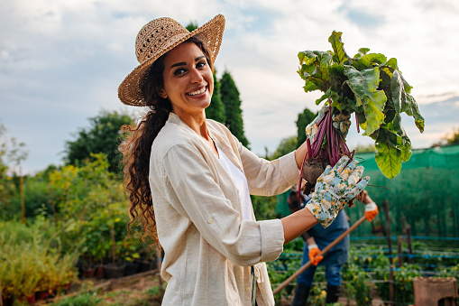 Happy young Caucasian woman standing in her and her fathers garden, holding her organic beet and smiling