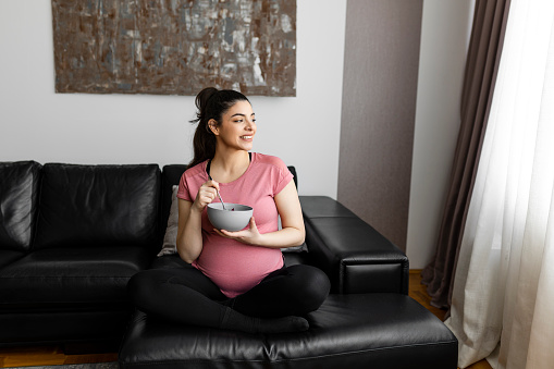 Smiling pregnant woman eating healthy salad at home