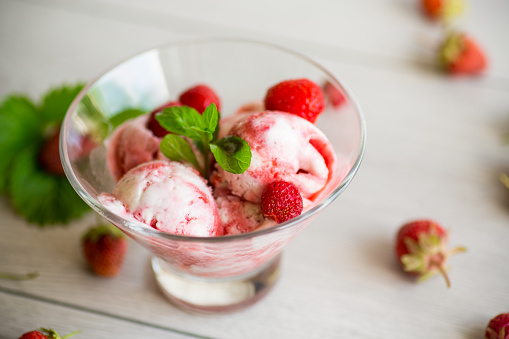 Balls of homemade strawberry ice cream in a bowl on a wooden table.