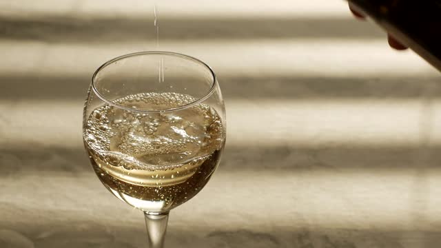White wine from a bottle is poured into a wine glass