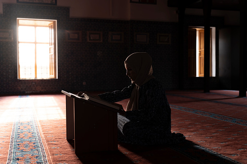 Woman Muslim reciting the Quran in a mosque. A woman praying in a mosque is a Muslim.