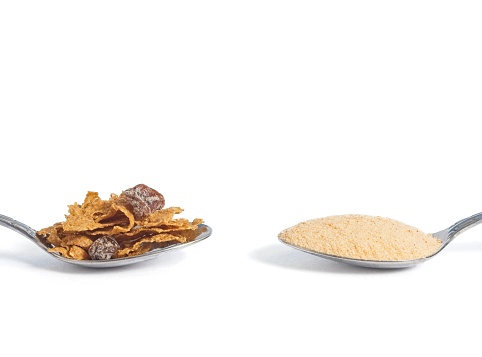 Choosing the way to get your fiber, dietary changes with food or powder supplements. Two spoons with a helping of bran cereal or psyllium husk powder.