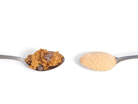 Choosing the way to get your fiber, dietary changes with food or powder supplements. Two spoons with a helping of bran cereal or psyllium husk powder.