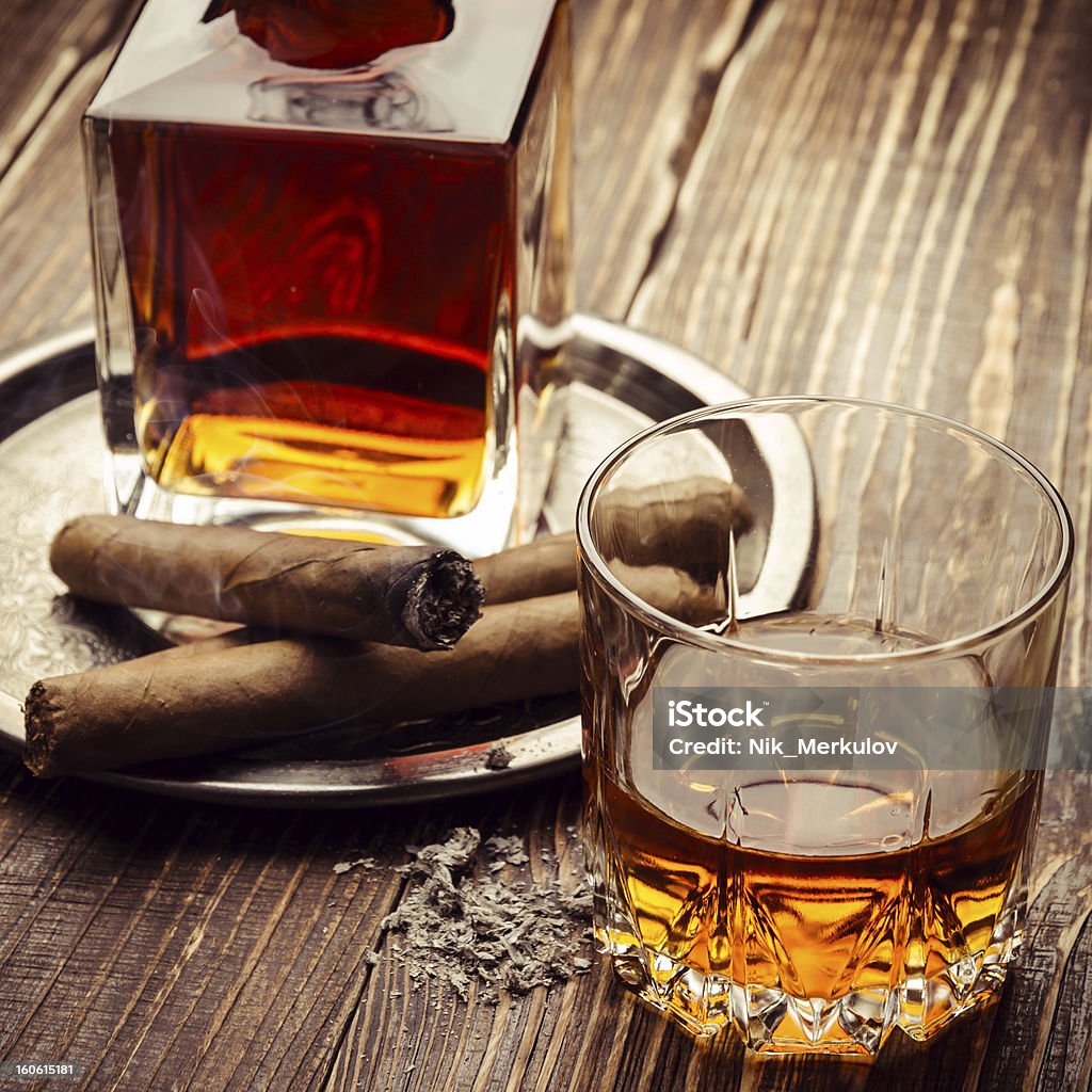 Vintage cognac and a burning cigar next to it Glass of cognac and cigars on wooden background Adult Stock Photo
