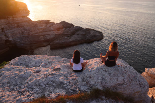 istock Back view of athletic women meditating on rock 1606153789