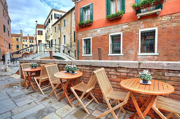 Wooden tables on narrow street among typical colorful houses and small bridge in Venice, Italy.