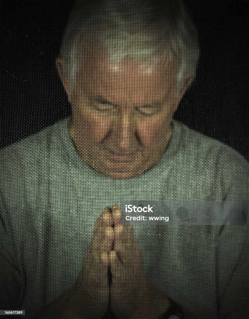 Man In Chuch Confessional A man in a dark screened Catholic Church confessional booth. Dark lighting. Selective focus on the screen. Adult Stock Photo