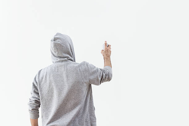 Graffiti artist with his hood up spraying a blank wall