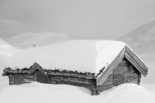 Old traditional Norwegian wooden log cabin house covered with snow during the winter.