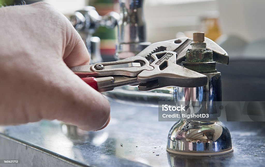 Plumber Real life situation - A plumber uses adjustable grips to remove a worn insert from a set of kitchen taps with a view to replace the damaged part. Faucet Stock Photo