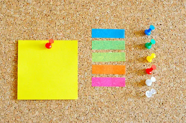 Photo of Cork board with yellow Post-it, multi color tape and pins