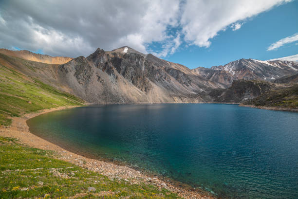 istock Deep mountain lake of phantom blue color among high mountains with pointed peak in changeable weather. Wonderful dramatic view to deep blue mountain lake among sunlit sharp rocks under cloudy sky. 1606317607